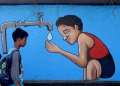 Mumbai: Two boys walk past a graffiti wall depicting a boy drinking water from a tap on the eve of World Water Day, in Mumbai on Tuesday, March 21, 2023. (Photo:IANS)