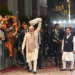 New Delhi: Prime Minister Narendra Modi waves a "gamcha" as he arrives during the celebration of NDAs victory in the Bihar Assembly elections, at BJP headquarters, in New Delhi, Friday, Nov. 14, 2025. Union Health Minister and BJP National President JP Nadda is also seen. (IANS)